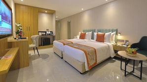 A hotel room with a large bed, a desk with a TV, a small kitchenette, and a seating area with a table and chairs.