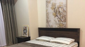 A bedroom with a bed, a nightstand, a framed picture, a painting, and a striped rug. - Cozy 1-bedroom condo with AC, WiFi in adorable Pasay City accross NAIA 3 RW (Pasay City)