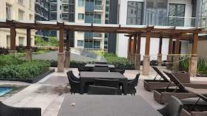 A rooftop patio with outdoor furniture, a swimming pool, and modern buildings in the background. - Cozy 1-bedroom condo with AC, WiFi in adorable Pasay City accross NAIA 3 RW (Pasay City)