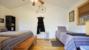 A room with two beds, a wooden bench, a radiator, and a ceiling fan.
