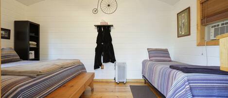 Una habitación con dos camas, un banco de madera, un radiador y un ventilador de techo.