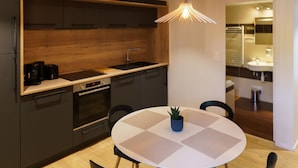 A modern kitchen with dark cabinets, a wooden countertop, and a built-in oven. There's a round table with a potted plant and chairs.