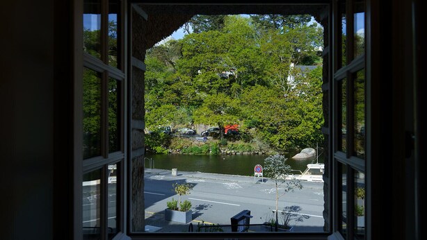A view through a window with a clear view of a road, a no parking sign, and a body of water with trees and parked cars in the background.