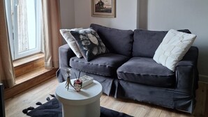 Un salon moderne avec un canapé gris, une petite table basse blanche et deux œuvres d’art encadrées accrochées au mur.