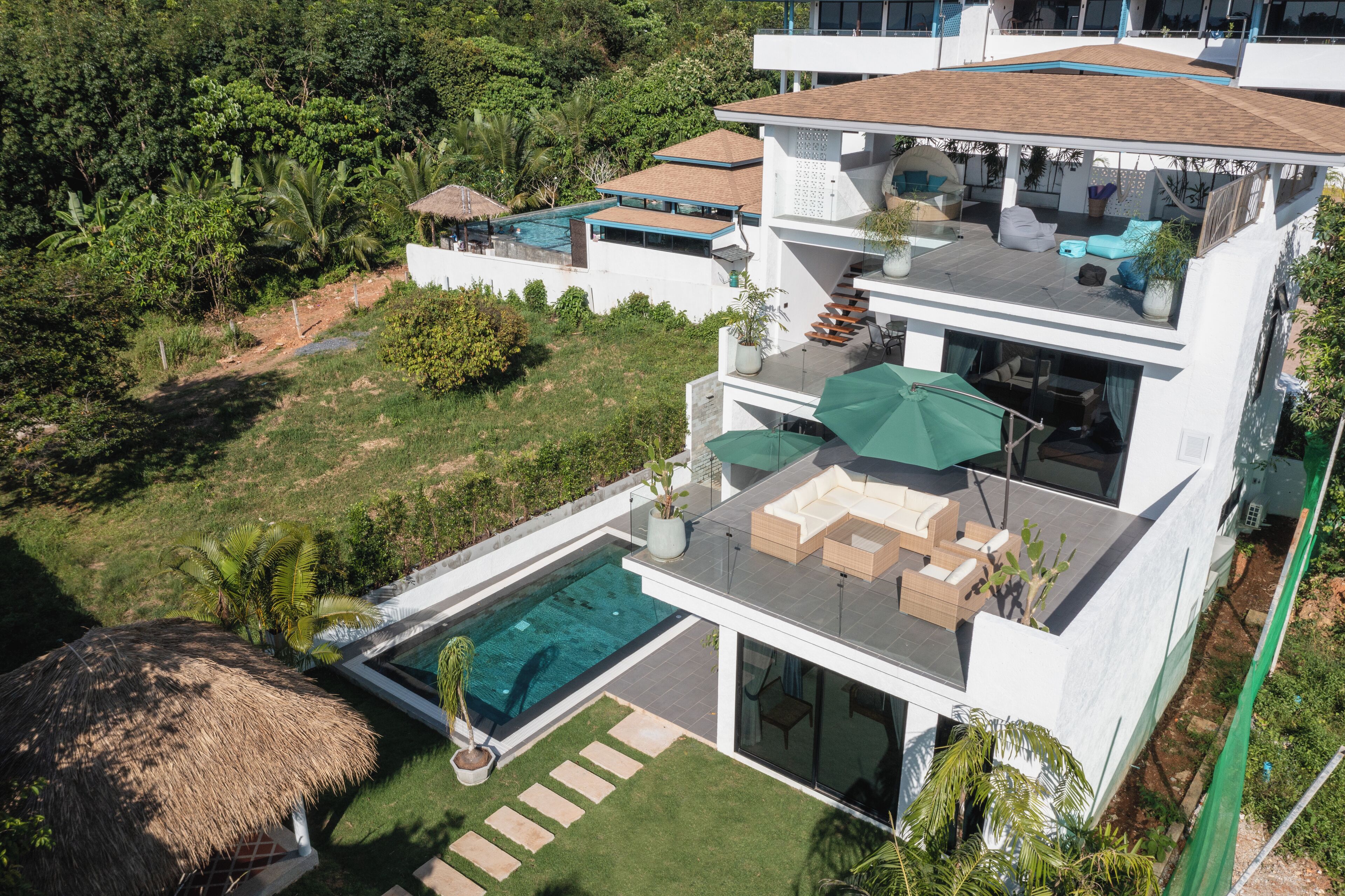 A modern two-story house with a swimming pool, outdoor seating, and lush greenery.