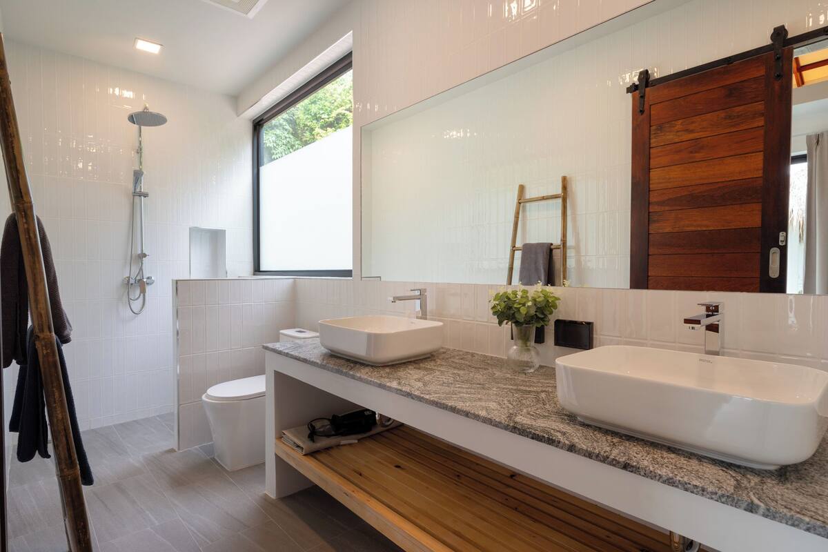 A modern bathroom with two sinks, a shower, and a large mirror.