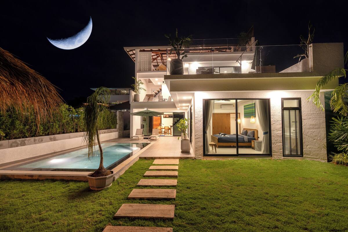 A modern house with a swimming pool, a staircase leading to a balcony, and a large window overlooking the pool.