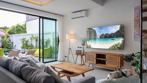A modern living room with a large TV, comfortable seating, and a view of a tropical beach. - The Guu Villas (Ko Lanta)