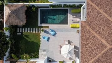 An aerial view of a modern outdoor pool area with a rectangular pool, lounge chairs, and a seating area with umbrellas.