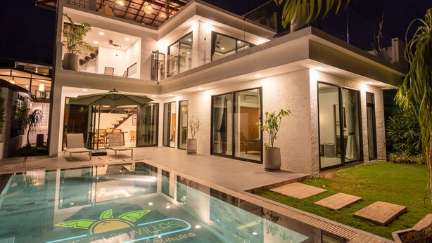 A modern two-story house with a swimming pool, glass doors, and a well-lit interior. - The Guu Villas (Ko Lanta)