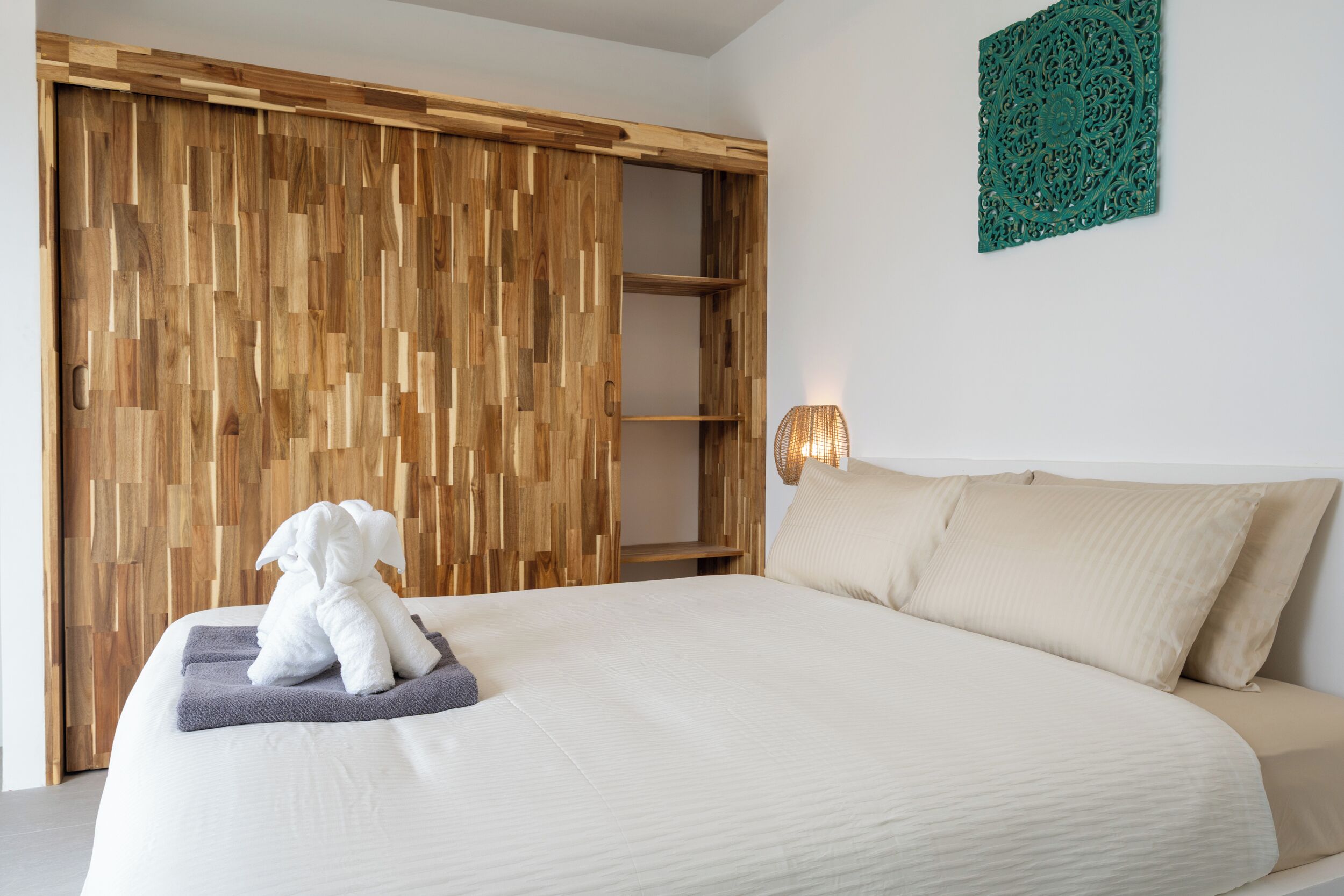 A bedroom with a wooden wardrobe, a bed with white bedding, and a wall-mounted decorative piece.