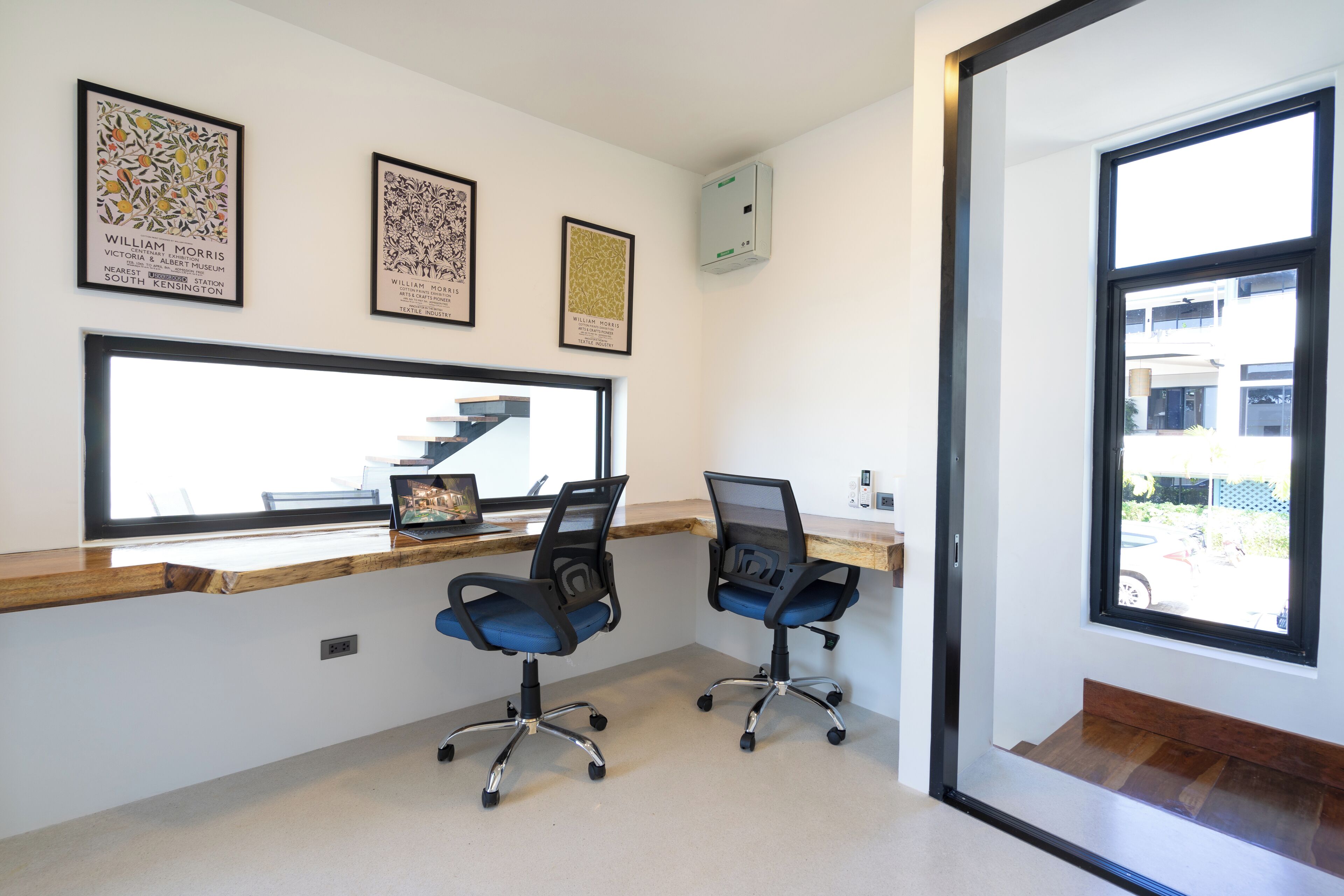 A modern office space with two blue office chairs, a wooden desk, and framed artwork on the wall.
