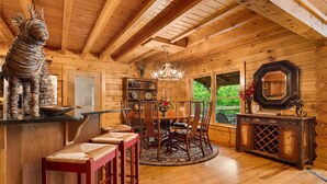 Het interieur van een houten chalet met een eethoek, een kroonluchter en een groot raam.