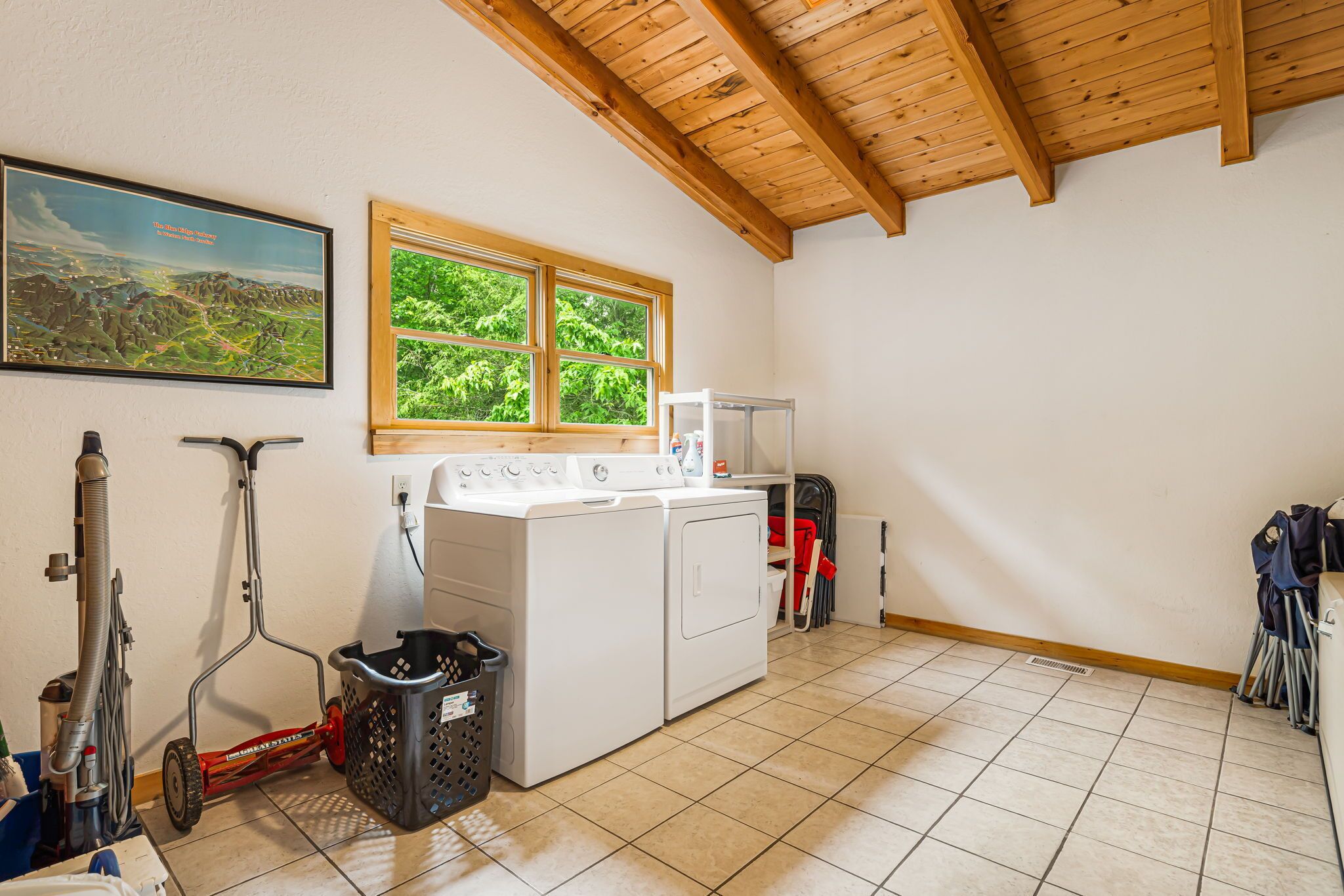 A laundry room with a washing machine, dryer, and a window with a view of greenery.