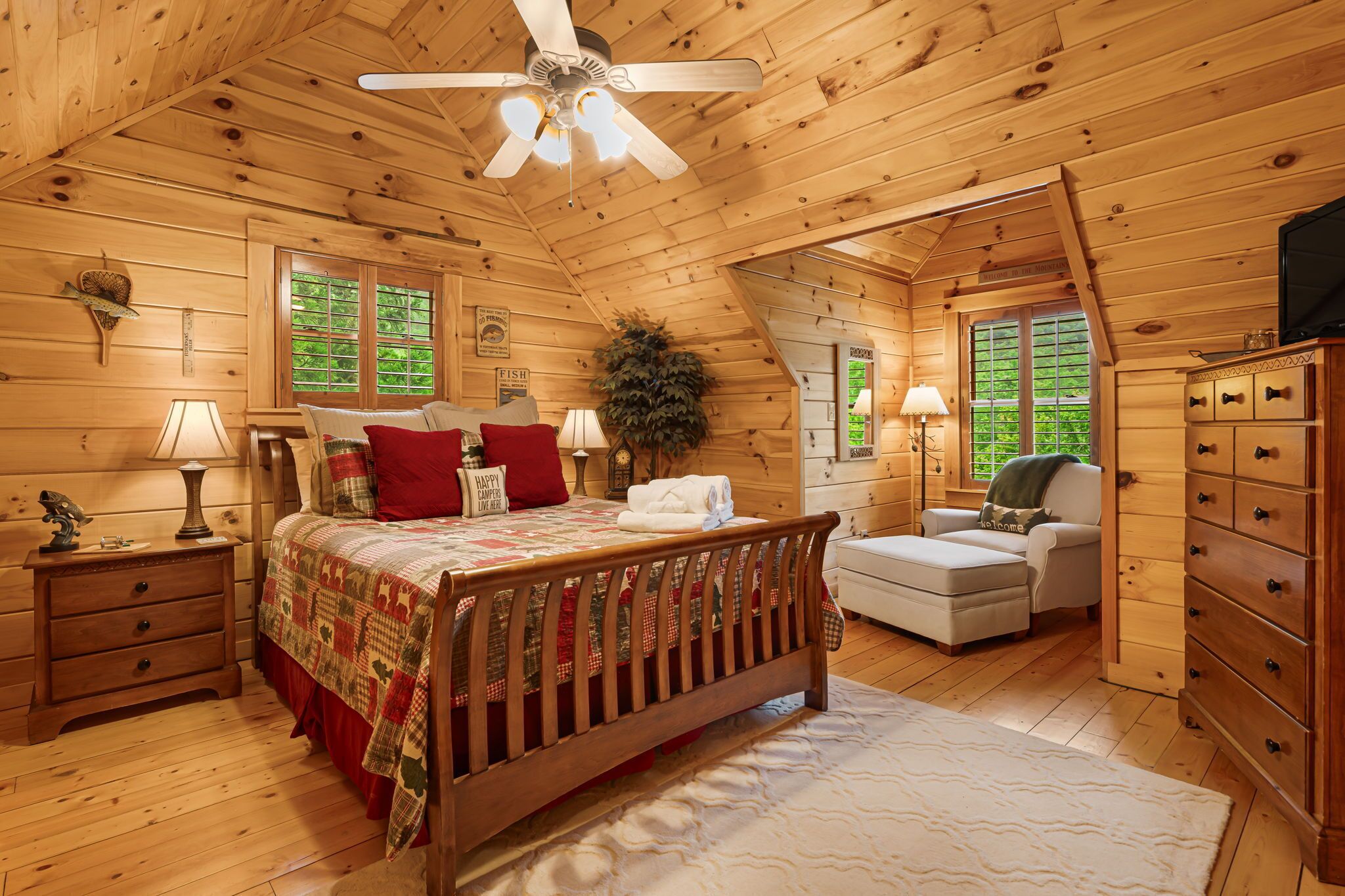 A cozy log cabin bedroom with a wooden bed, a desk, a chair, and a dresser.
