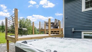 Ein Whirlpool auf einer Holzterrasse mit Blick auf ein Haus und Bäume.