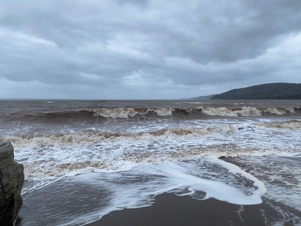 A beach with waves crashing onto the shore under a cloudy sky.