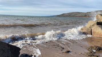 En strand där vågorna slår in mot land, omgiven av ett stenigt landskap och avlägsna kullar.