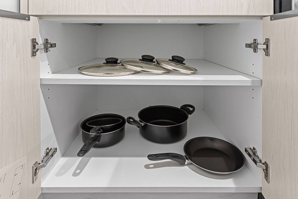 A kitchen cabinet with three pots and pans on the lower shelf and two lids on the upper shelf.