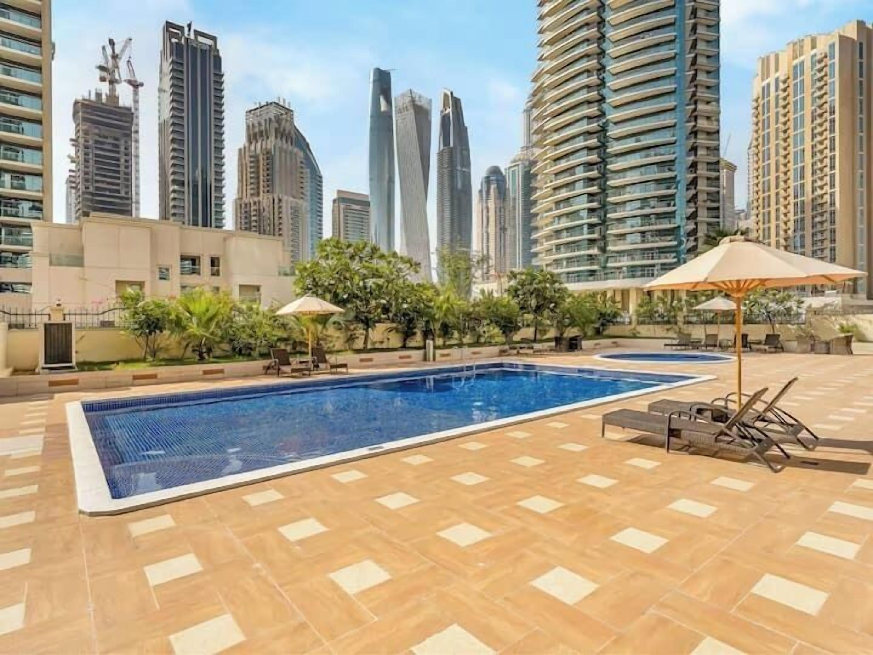 A rooftop pool with lounge chairs and umbrellas, surrounded by high-rise buildings.