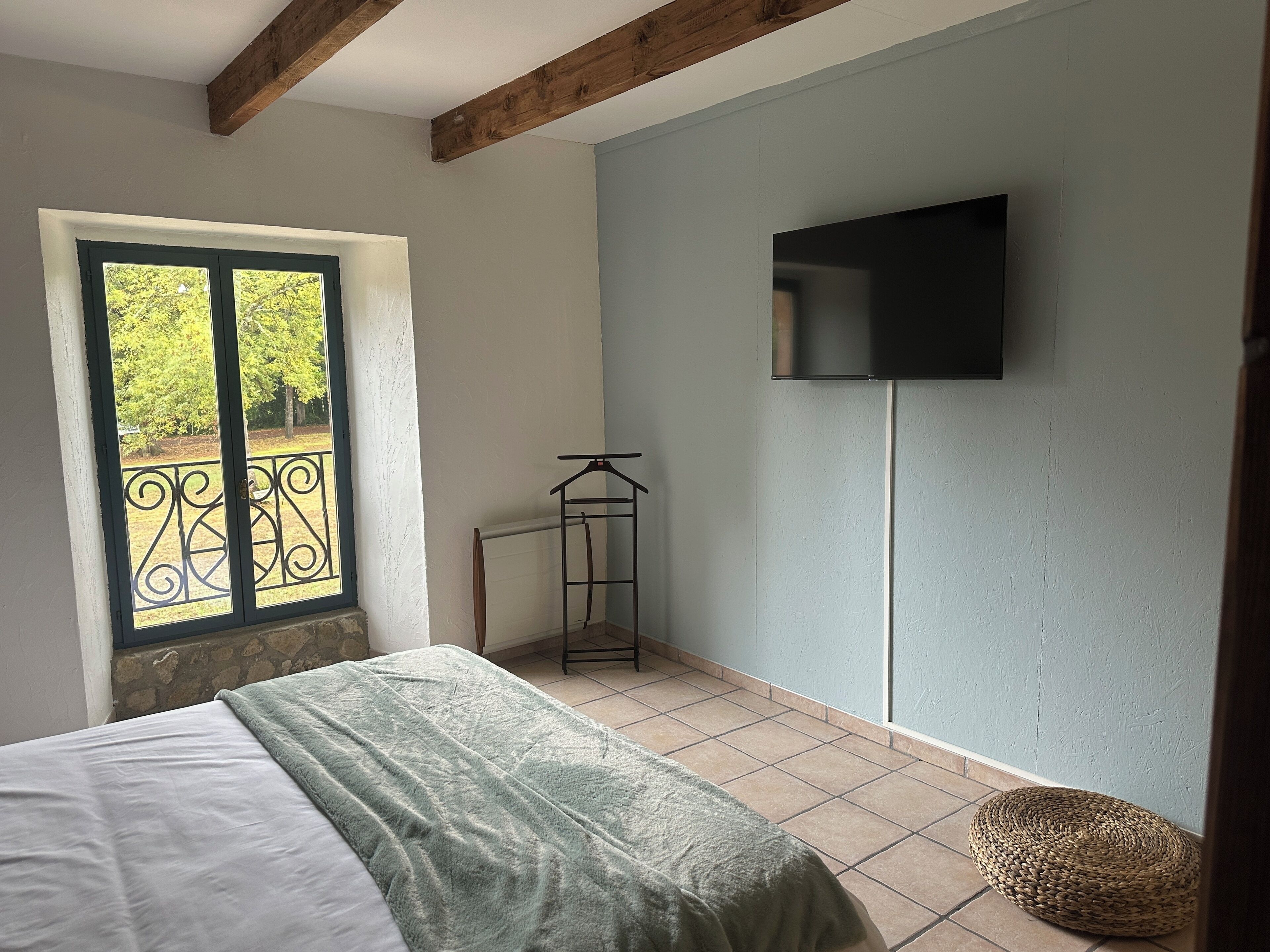 A bedroom with a bed, a window with a view, a TV mounted on the wall, and a woven basket on the floor.