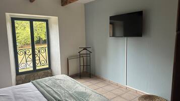 A bedroom with a bed, a window with a view, a TV mounted on the wall, and a woven basket on the floor.