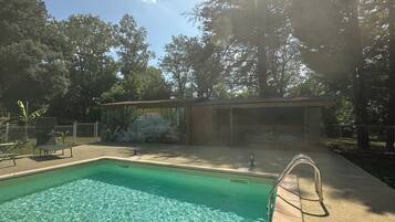 Una piscina con un mural, rodeada de árboles y un área de descanso cubierta.