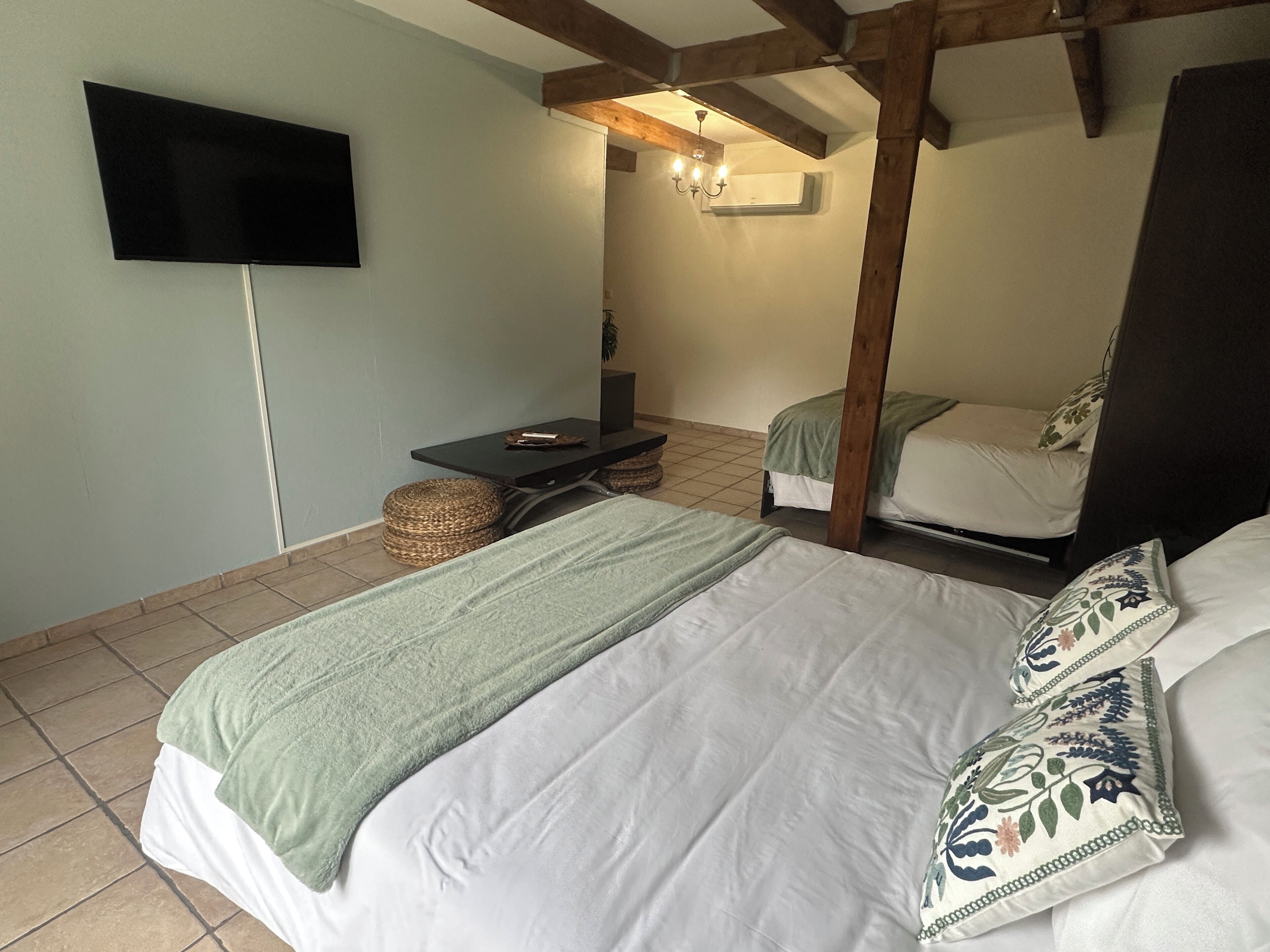Une chambre avec deux lits, un téléviseur à écran plat fixé au mur, une petite table et un panier en osier.