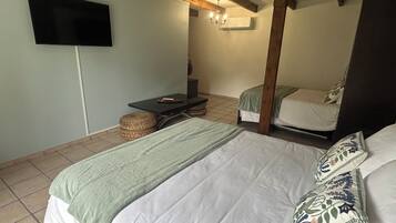 Une chambre avec deux lits, un téléviseur à écran plat fixé au mur, une petite table et un panier en osier.