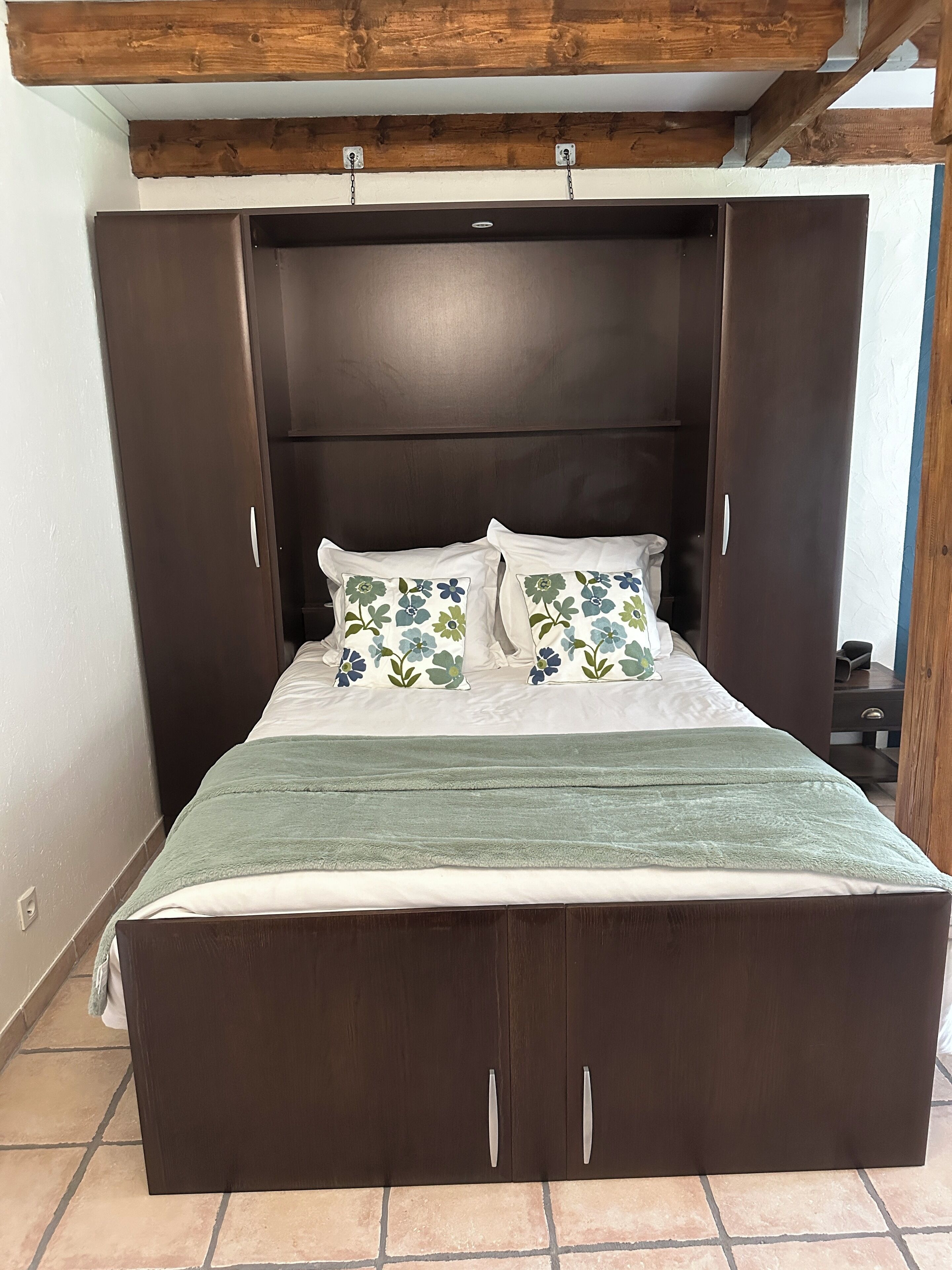 A bed with a dark headboard, two floral pillows, and a green blanket.