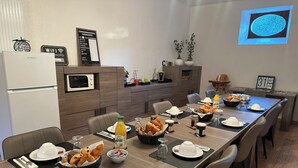 Un coin repas avec une longue table dressée pour le petit-déjeuner, comprenant des croissants, du pain et diverses boissons.