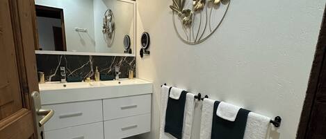 A bathroom with a white sink, a mirror, and a decorative wall piece.