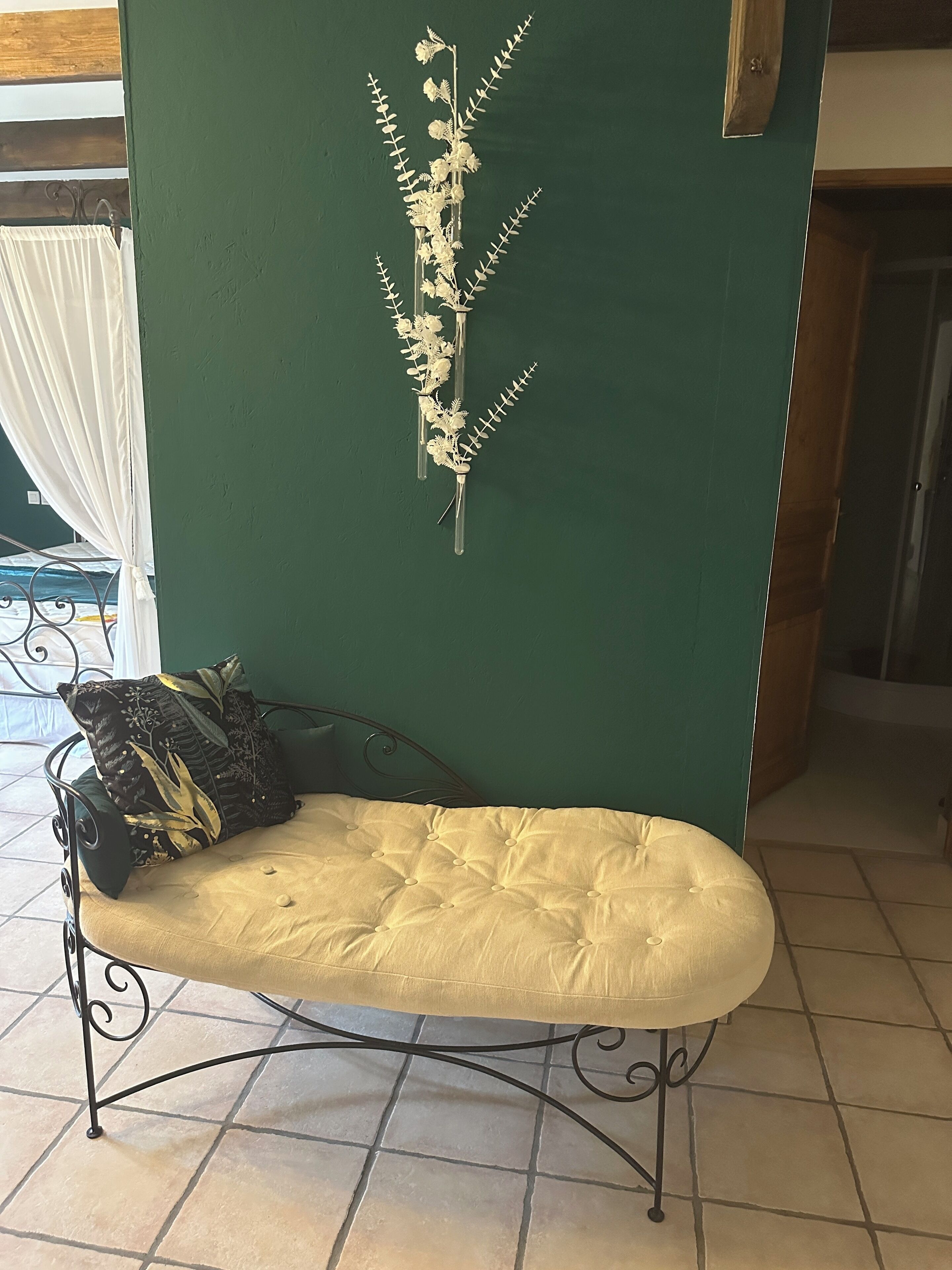 A green wall with a decorative plant arrangement, a cushioned bench with a patterned pillow, and a metal-framed chair.