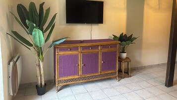 Una habitación con un armario de mimbre morado, un televisor montado en la pared y una planta en maceta.