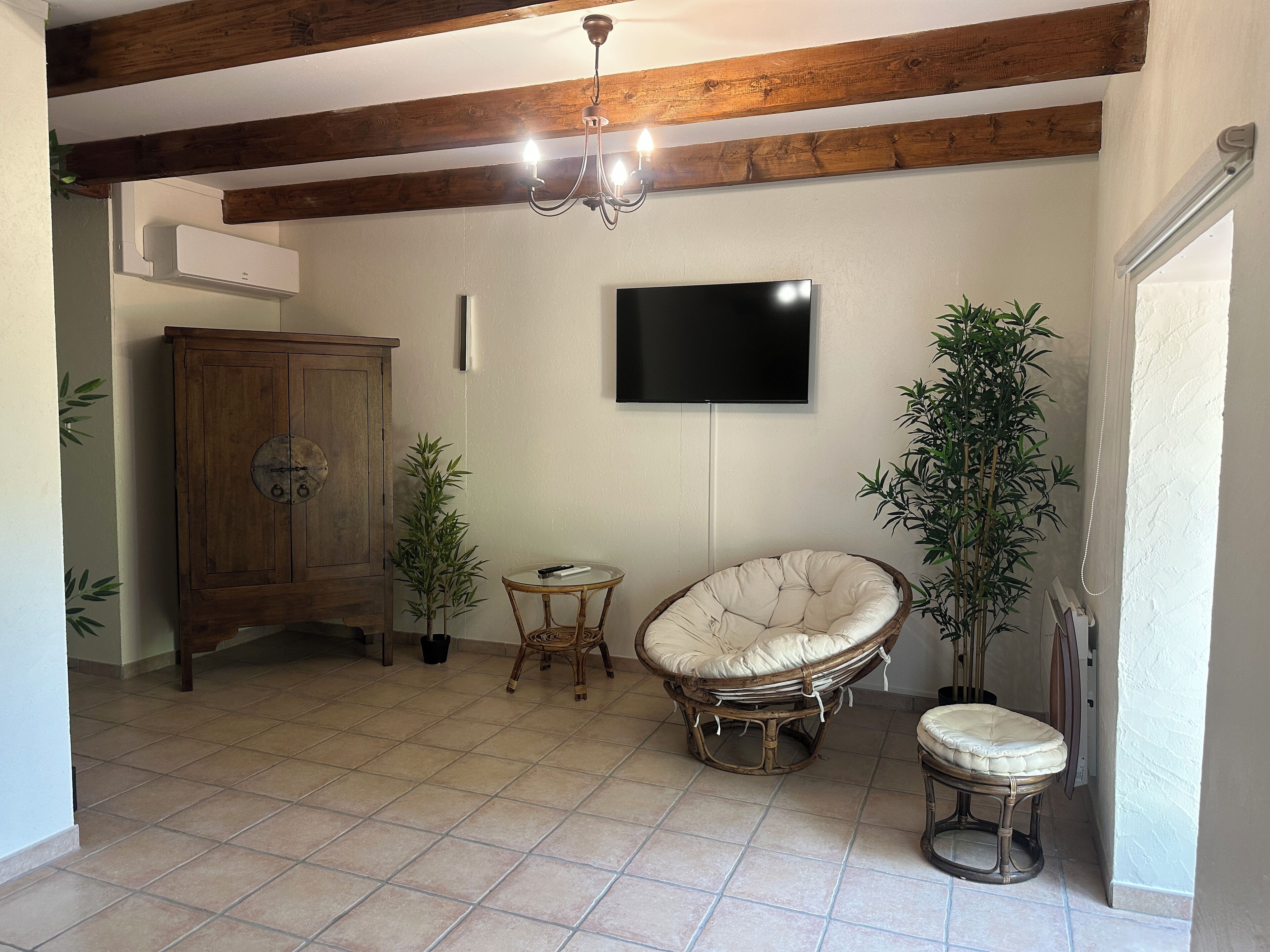Habitació amb sostre de fusta, televisió penjada a la paret, cadira de vimet, taula petita i un armari.