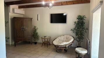 Habitació amb sostre de fusta, televisió penjada a la paret, cadira de vimet, taula petita i un armari.