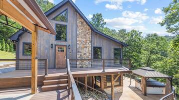 A modern wooden house with a stone facade, a deck, and a covered outdoor seating area.