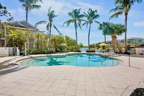 A swimming pool with palm trees, a building with a flat roof, and a clear sky. - Resort-style Condo with Pool and Water Views! Near Anna Maria Islands beach (Bradenton)