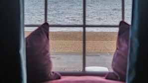 Ein Fenster mit Blick auf Meer und Strand, eine Fensterbank mit Kissen und ein Blick in den Himmel.