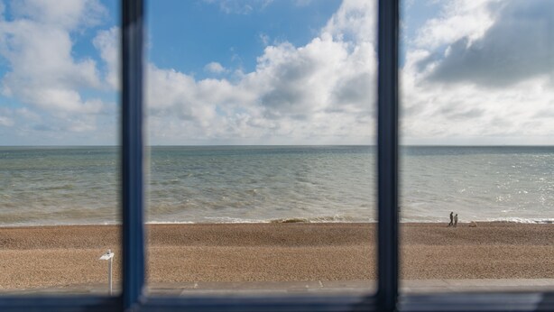 Blick auf einen Strand durch ein Fenster, mit Meer und Himmel.