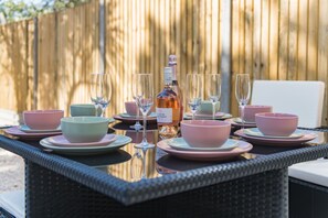 A table set with pink and green bowls, wine glasses, and a bottle of wine, with a wooden fence in the background. - Brook Cottage, Whitstable (Whitstable)