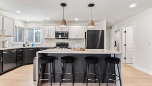 A modern kitchen with white cabinets, a central island with stools, stainless steel appliances, and pendant lighting. - 5 Bedroom house in prime location by the village (Meridian)