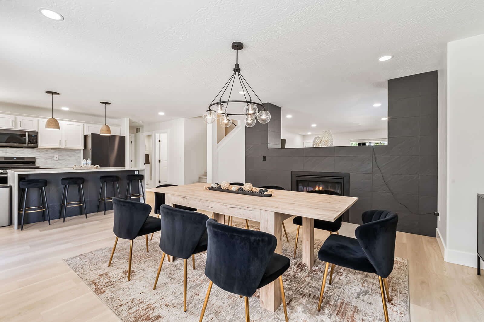 A modern kitchen with a dining area, featuring a wooden table, black chairs, and a chandelier.