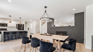 A modern kitchen with a dining area, featuring a wooden table, black chairs, and a chandelier. - 5 Bedroom house in prime location by the village (Meridian)
