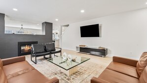 A modern living room with a fireplace, leather sofas, a glass coffee table, and a flat-screen TV mounted on the wall. - 5 Bedroom house in prime location by the village (Meridian)