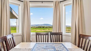 A table with a crossword puzzle in a room with two windows, wooden chairs, and a view of a green landscape.