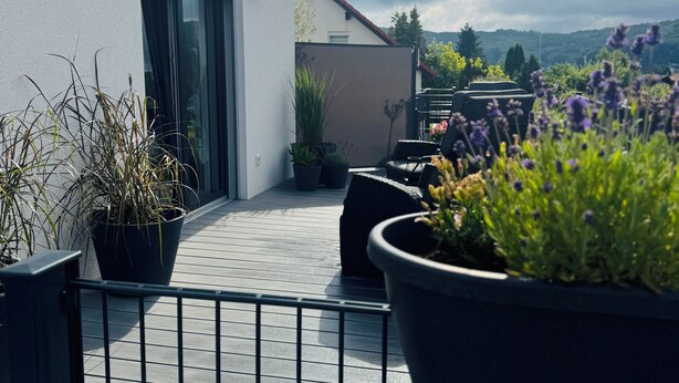 A rooftop terrace with potted plants, a metal railing, and a view of a mountain range. - Beautiful, sun-drenched vacation apartment on the Dünsberg - surrounded by greenery (Biebertal)