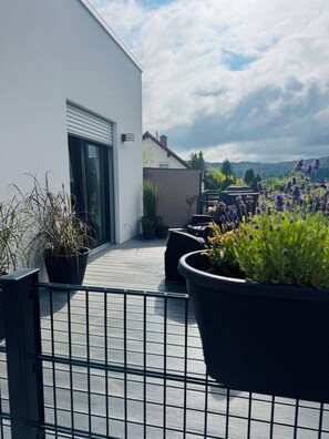 A rooftop terrace with potted plants, a metal railing, and a view of a mountain range. - Beautiful, sun-drenched vacation apartment on the Dünsberg - surrounded by greenery (Biebertal)