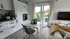 A modern kitchen with white cabinets, a dining table, and a sofa. - Beautiful, sun-drenched vacation apartment on the Dünsberg - surrounded by greenery (Biebertal)