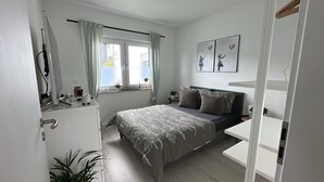 A bedroom with a bed, bedside table, and a window with curtains. - Beautiful, sun-drenched vacation apartment on the Dünsberg - surrounded by greenery (Biebertal)